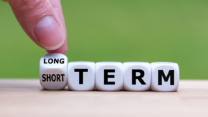 Dice showing words representing long-term and short-term financial goals in the context of tax loss harvesting, alongside an initial planner from Ballentine Capital Advisors, a financial planner in Greenville, SC.
