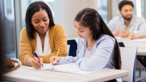  A woman assisting a young girl in filling out forms, symbolizing guidance in navigating the FAFSA process. The image highlights the importance of working with a financial advisor in Greenville, SC, to maximize financial aid opportunities, adapt to FAFSA changes in 2025, and align education funding with long-term financial goals.