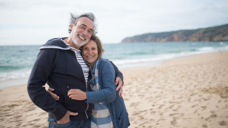 Smiling couple embracing on a sunny beach, representing the benefits of strategic retirement planning and financial independence